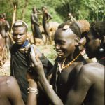 A Suk (Pokot) porter, working with a British forestry survey team, looks at his reflection in the shaving mirror of Henry Osmaston (Working Plans Officer, Uganda Forest Department) on a safari to the Karasuk hills, Kenya, May 1959 © British Empire and Commonwealth Collection at Bristol Archives 2001/291/1/4/III/82 (Lang Brown Collection) Image: Looking the part: A Suk (Pokot) porter, working with a British forestry survey team, looks at his reflection in the shaving mirror of Henry Osmaston (Working Plans Officer, Uganda Forest Department) on a safari to the Karasuk hills, Kenya, May 1959 © British Empire and Commonwealth Collection at Bristol Archives 2001/291/1/4/III/82 (Lang Brown Collection)