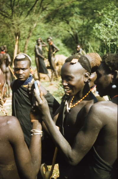 Image: Looking the part: A Suk (Pokot) porter, working with a British forestry survey team, looks at his reflection in the shaving mirror of Henry Osmaston (Working Plans Officer, Uganda Forest Department) on a safari to the Karasuk hills, Kenya, May 1959 © British Empire and Commonwealth Collection at Bristol Archives 2001/291/1/4/III/82 (Lang Brown Collection)